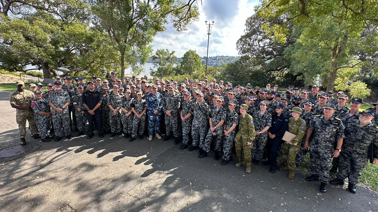 Navy and Army Australian together with international Cadets, alongside Officers and Staff, smiling for the camera on Cockatoo Island, Sydney Harbour